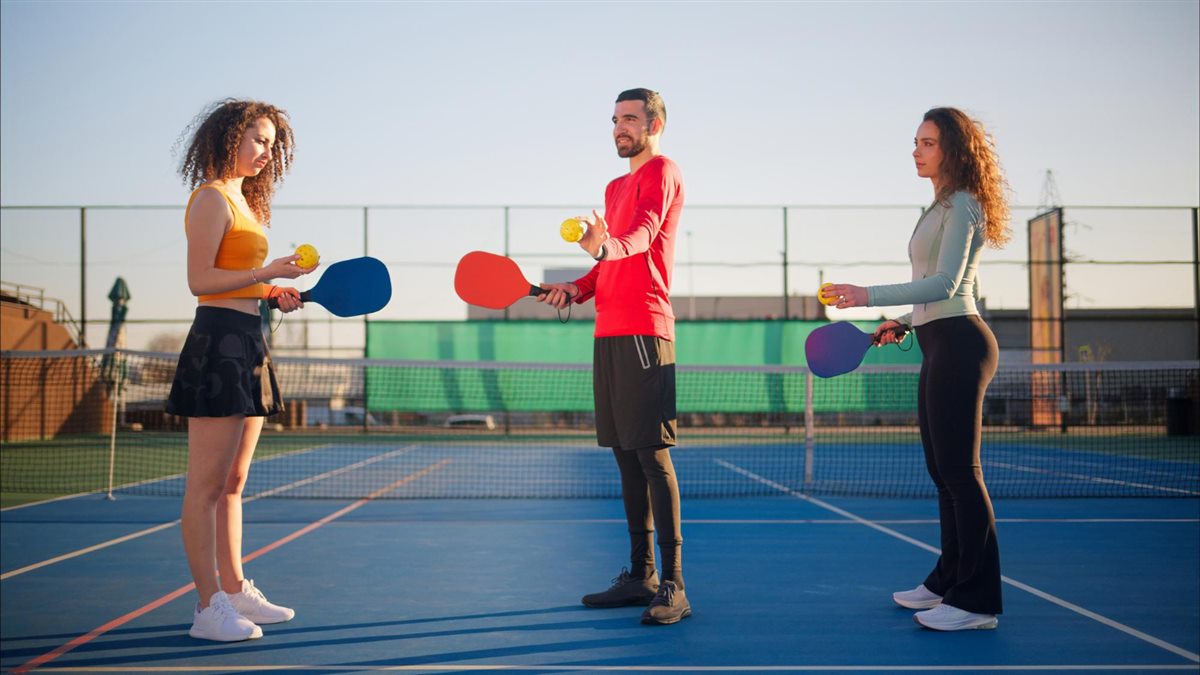 Three players with pickleball paddles meeting at the net